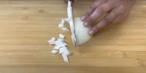 Close-up of hands chopping a white onion on a wooden cutting board.